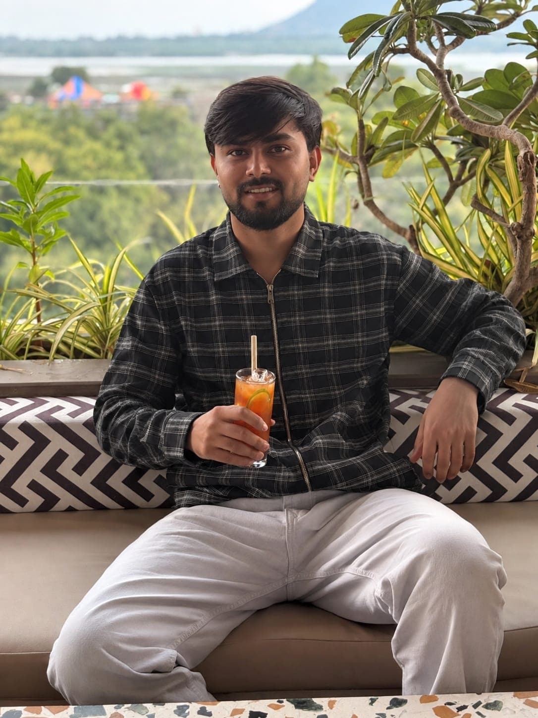 Kenil Kanani sitting on a terrace in a checked shirt, holding a glass.